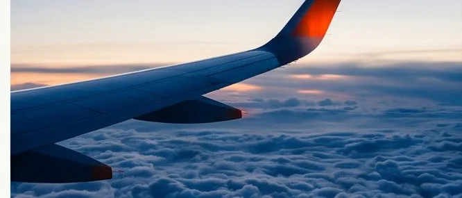Aircraft wing above clouds at dusk, orange wingtip